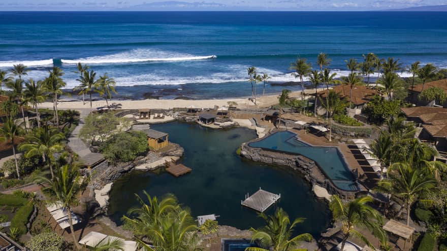 Aerial view of resort pool that mimics a curved pond, palm trees, beach and ocean