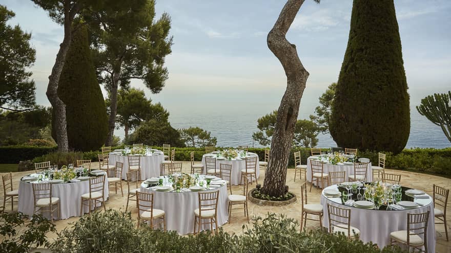 Small white tables in Les Terasses outdoor event space under tall trees