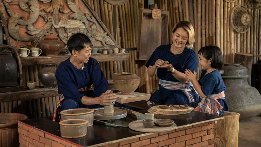 A potter teaching a woman and a child to shape clay in a rustic pottery workshop, surrounded by traditional tools and pottery.