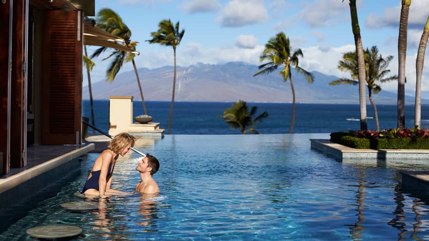 Man and woman at stools of swim-up bar in Serenity Pool, views of Lanai and the West Maui Mountains