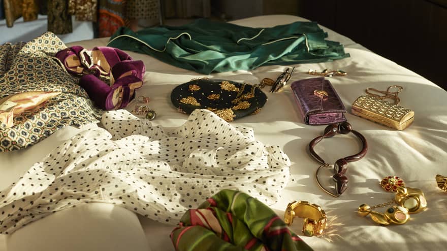 Clothes, gold jewelry and wallets spread out on bed.