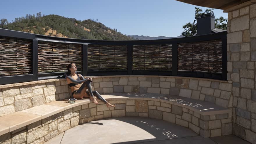 Woman slathered in mud sits on stone bench sun tanning during spa treatment
