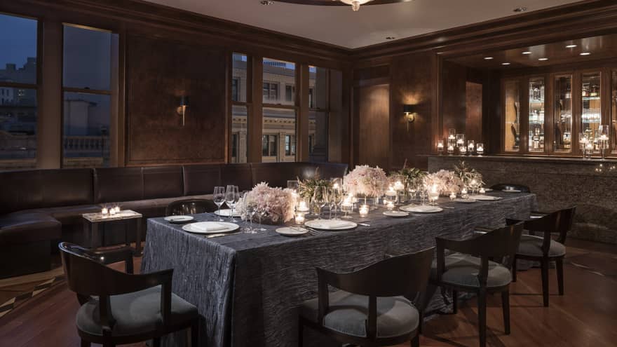 Elegant, candle-lit dining table in private den with grey tablecloth, pink flower arrangements, wine glasses