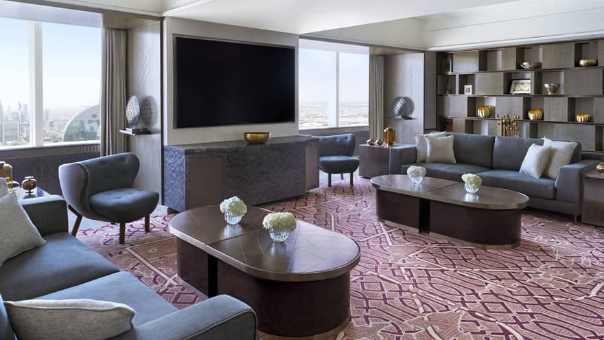 Living room with burgundy patterned carpet, two grey sofas, two coffee tables and TV