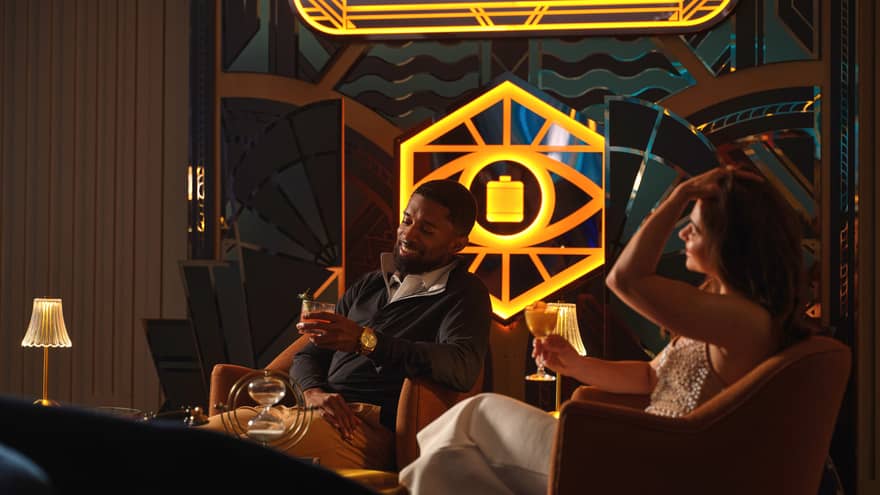 Two guests sitting in chairs beside a window and holding drinks