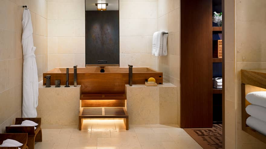 White bathrobe hanging in Master bedroom bathroom with wood Japanese soaking tub, marble ledge, tile walls