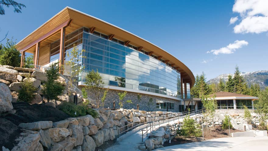 Exterior of Squamish Lil'Wat Cultural Centre with floor to ceiling windows, wooden roof, stone walls