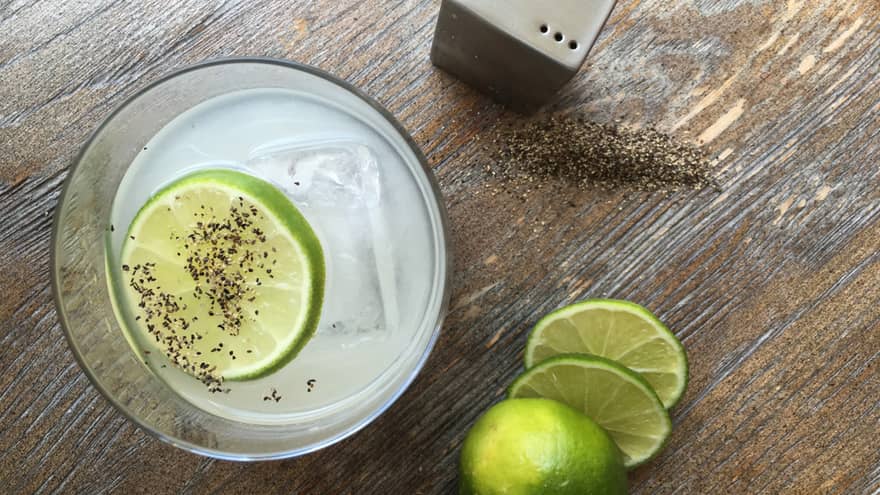 Lime wheel with black pepper, ice cube in rock glass