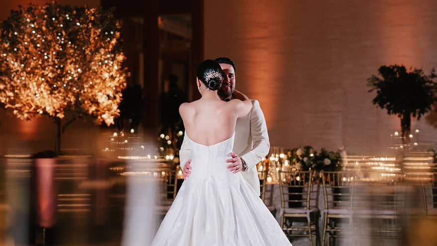 Bride and groom, both wearing white, dance in the centre of a ballroom dance floor