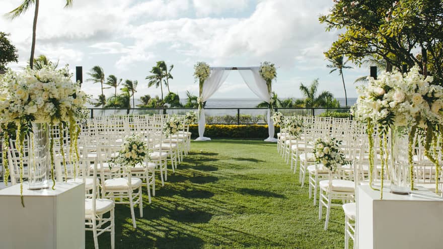 Outdoor wedding ceremony set up, rows of white chairs face altar on event lawn near ocean