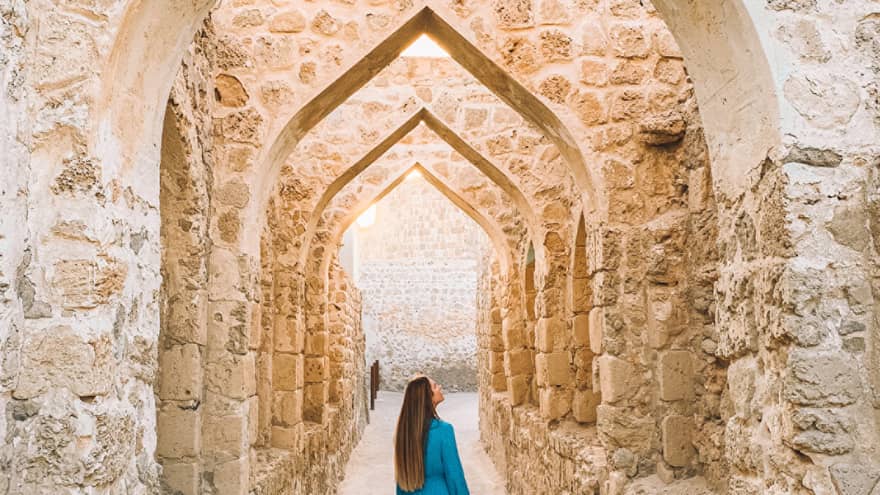 A woman stands underneath a stone pathway.