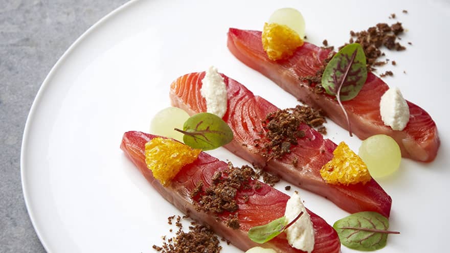 White plate with three thick slices of sashimi garnished with fruits, greens