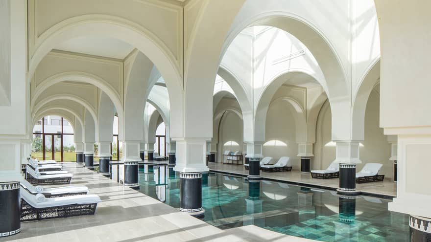 Arched white pillars, soaring ceilings over sunny indoor swimming pools, lounge chairs