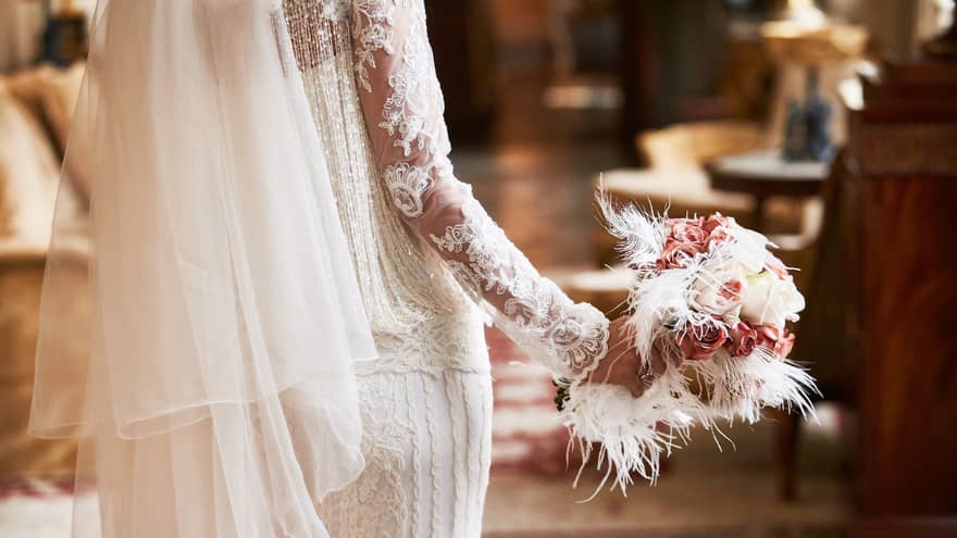 A close up of a bride's bouquet made up of white roses, pink flowers and white feathers
