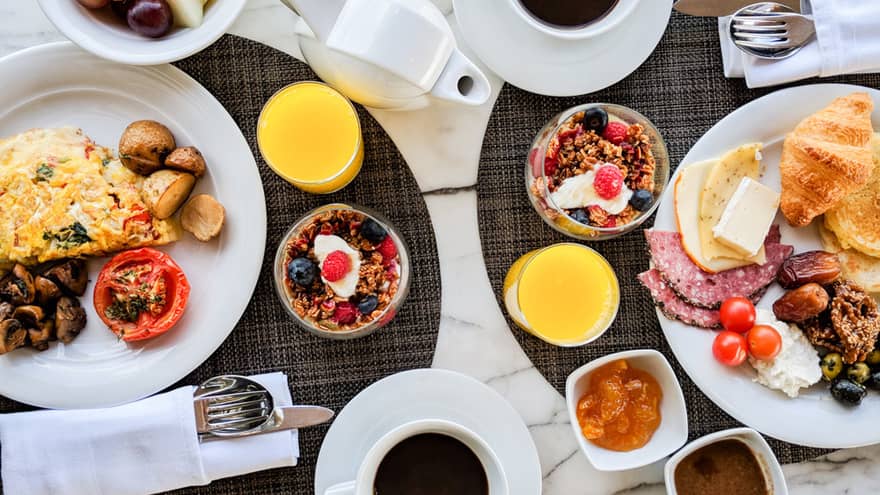 Aerial view of brunch table with omelette, cheeses, meats, croissants, cups of granola and yogurt