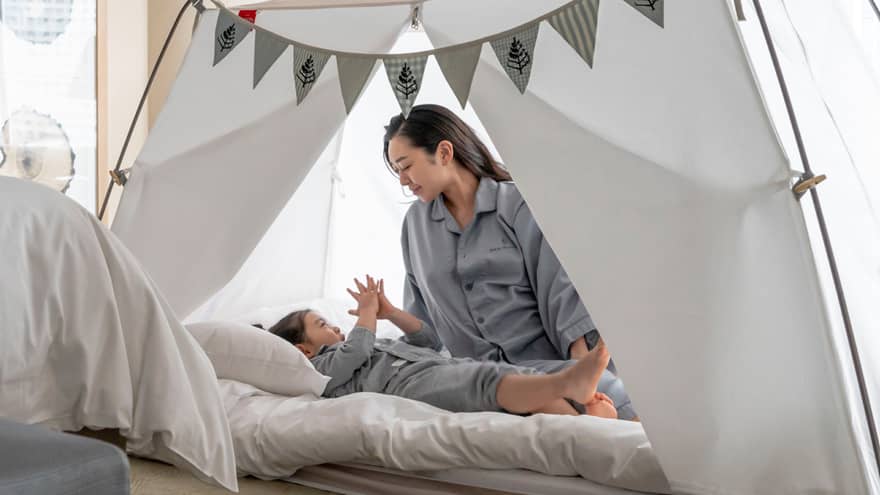 Parent and child in pyjamas playing together inside a cozy tent with bunting decorations