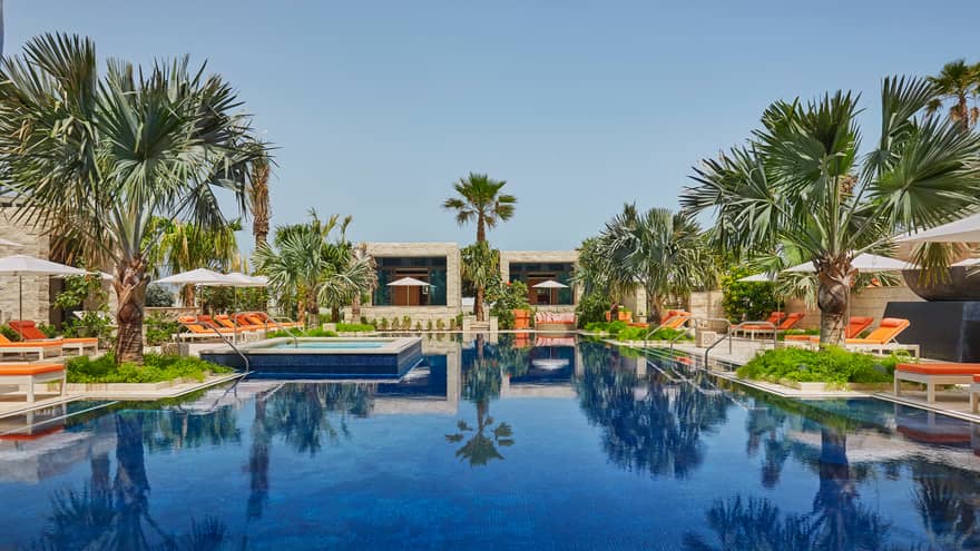 Azure adults-only swimming pool, surrounded by palm trees, orange lounge chairs, cabanas