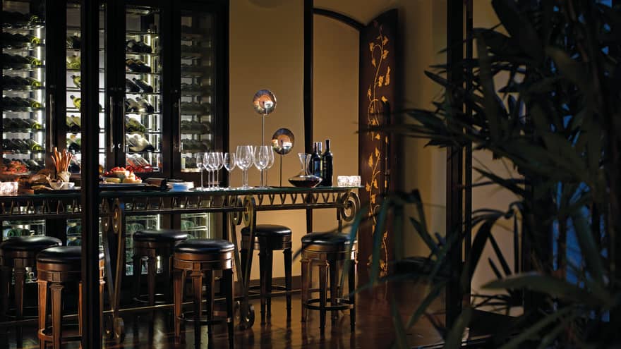 Wine bottle, glasses, cheese platter on table in front of wine cellar in dark restaurant