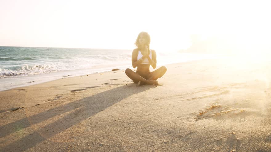 Woman in swimsuit sits cross-legged on sand beach at sunset