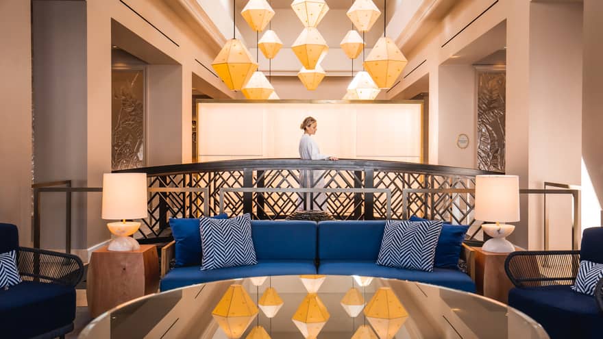 A woman walking behind a blue sofa in a lounge area with large geometric chandelier.