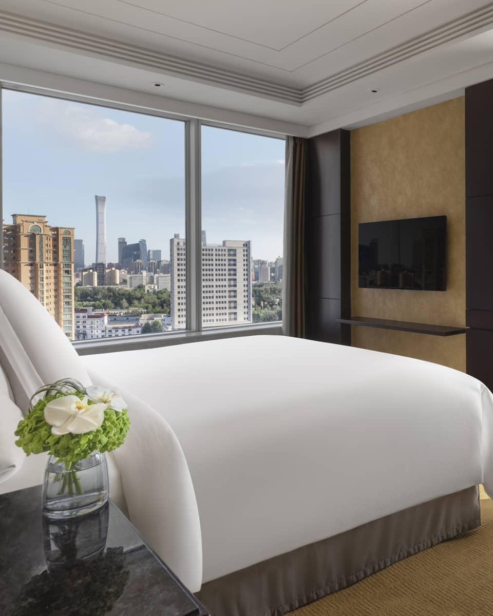 Hotel room with king bed, arm chair, wall-mounted TV and two walls of windows with river view
