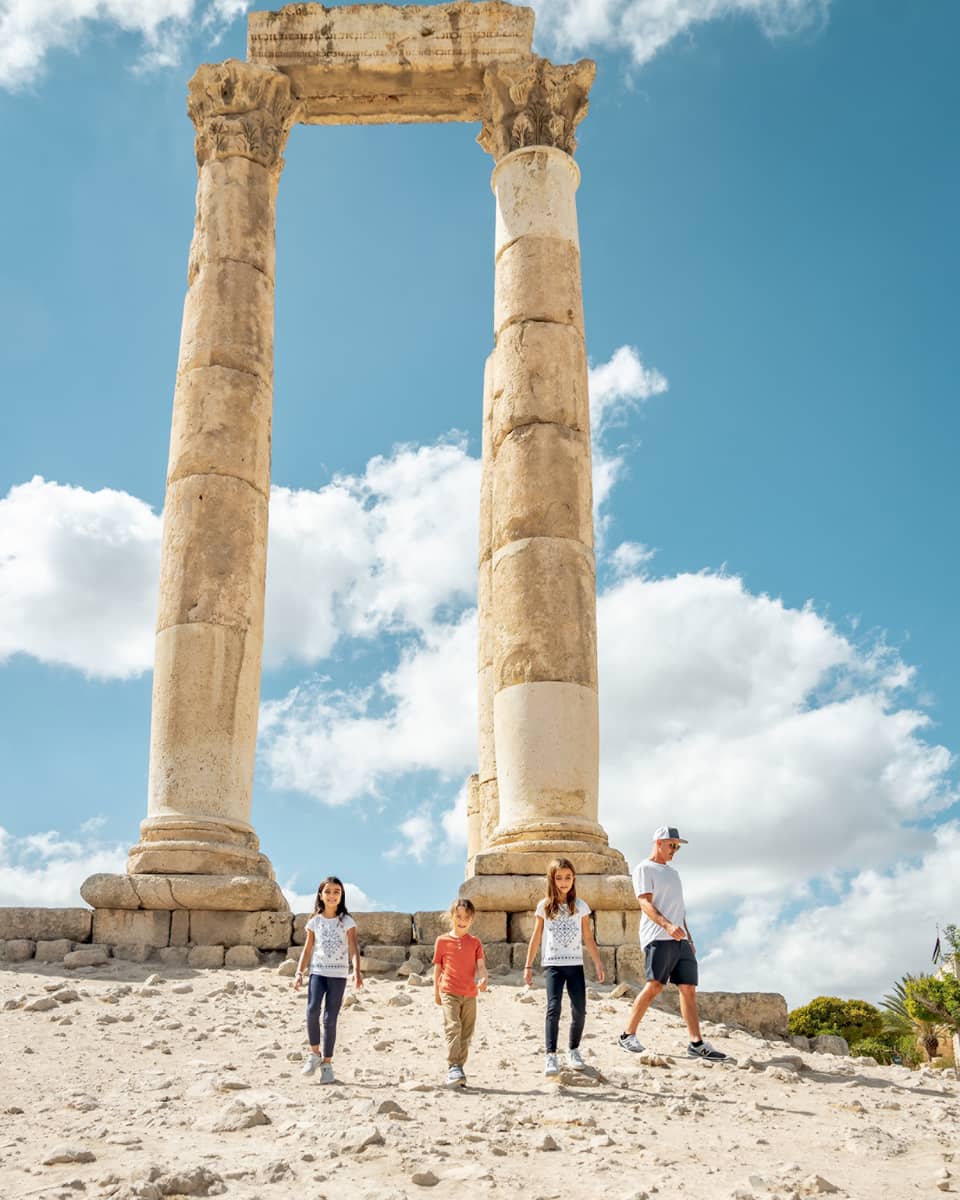 A parent and three children walk together next to the ruins of the Amman Citadel