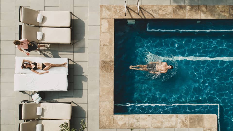 Woman laying in pool chair while man swims in pool.