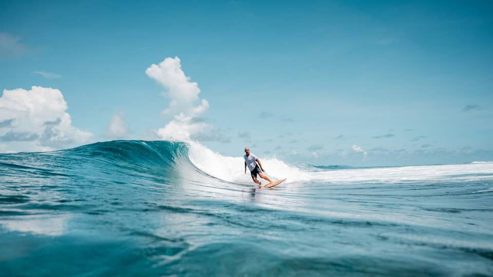 A person surfing a wave in the ocean, the water is a deep blue matched by the blue sky.