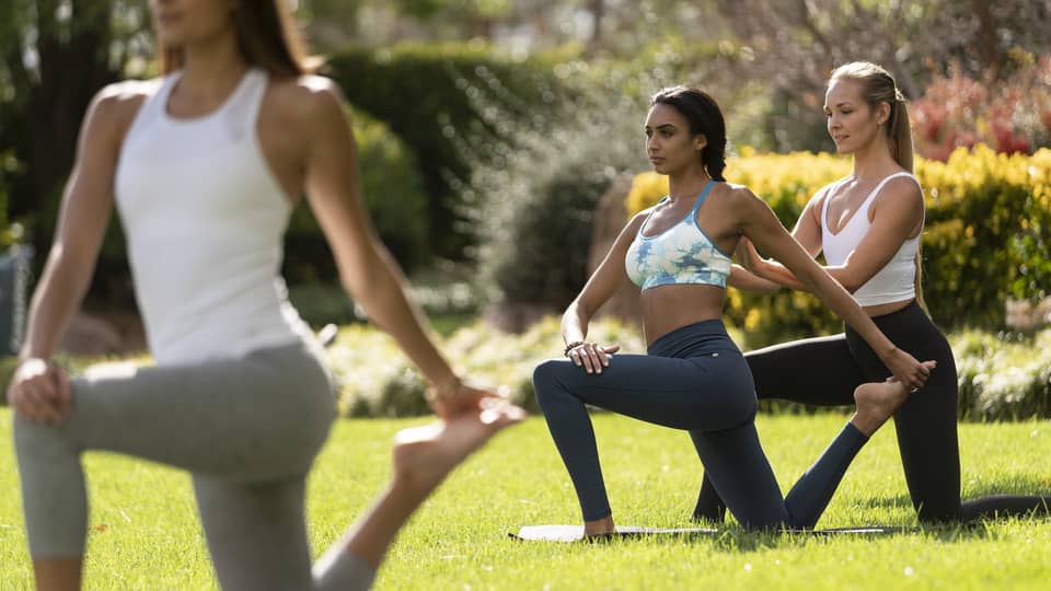 Three women doing yoga on grass outside.