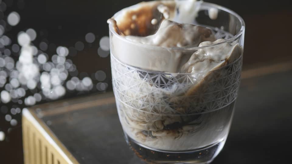 Stream of milk being poured into etched glass on dark bartop