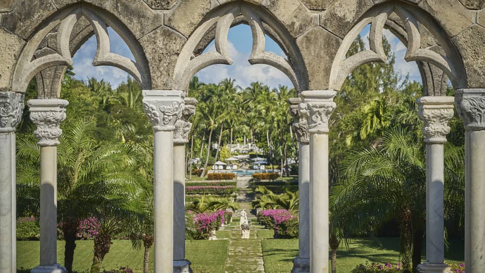 Ornate stone arch leading to a garden pathway with lush greenery, colourful flowers and a statue