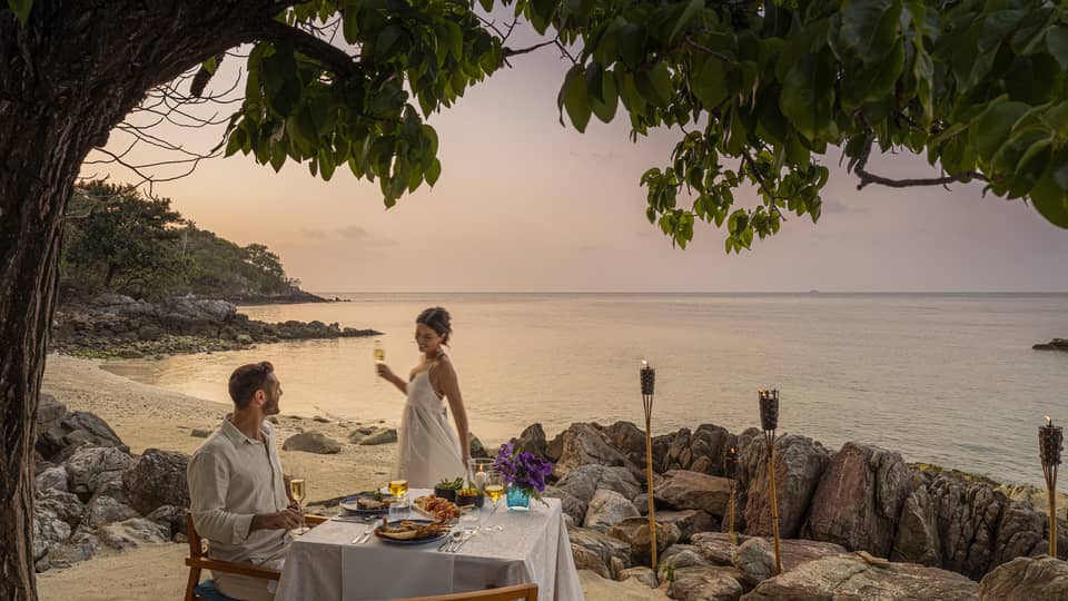 A beach dinner date at dusk, with a couple enjoying a serene seaside view.