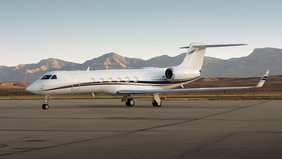 Private jet parked on a runway with mountain range in the background.