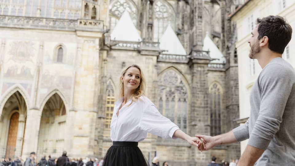 Couple smiling, holding hands with arms stretched as they tour historic city