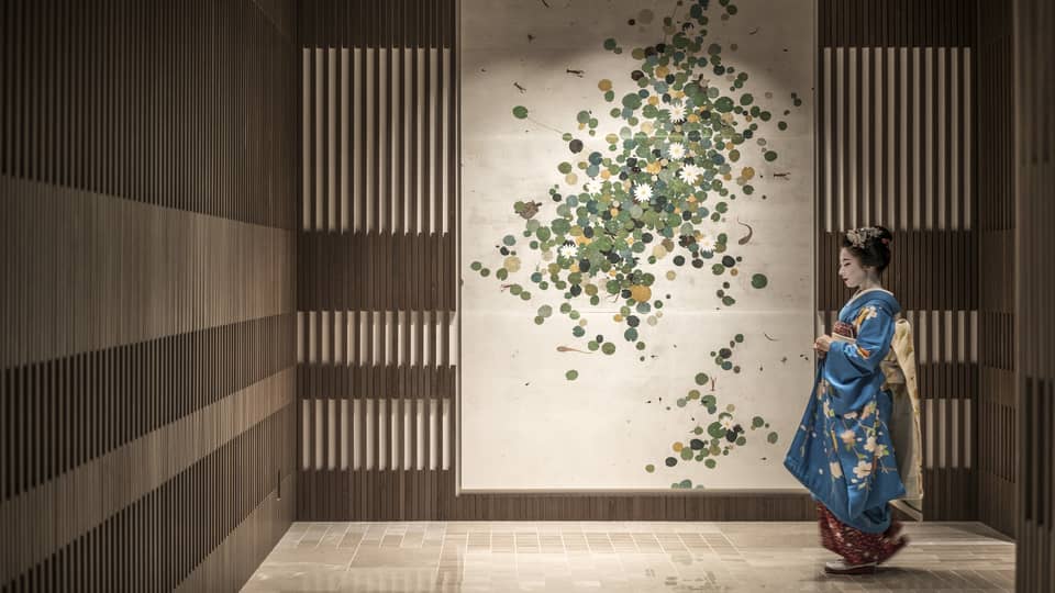 Person in a blue kimono with floral patterns standing in front of a wall decorated with a botanical art piece at Four Seasons