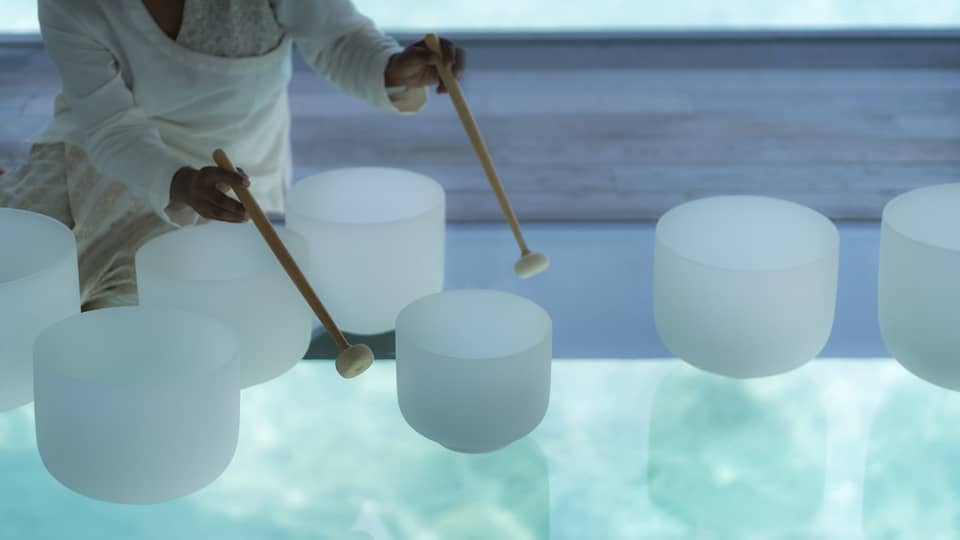 Spa staff plays various white crystal bowls with wood mallets during sound healing session