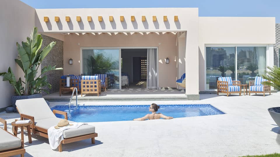 Female guest lounges in private pool at her beach villa, blue skies overhead