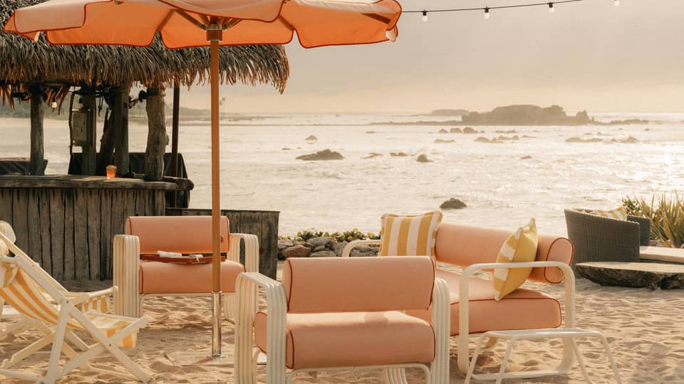 Light orange upholstered and fabric lounge chairs and sun umbrella on a beach with ocean and coastal views in the background