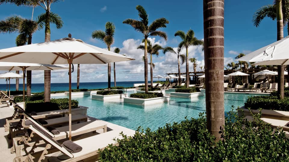 Aleta Pool with white potted palms, surrounded by white patio chairs, umbrellas, ocean views
