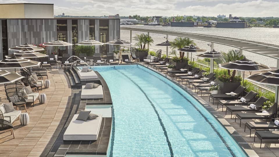 Pool with lounge chairs and umbrellas and a view of the river.