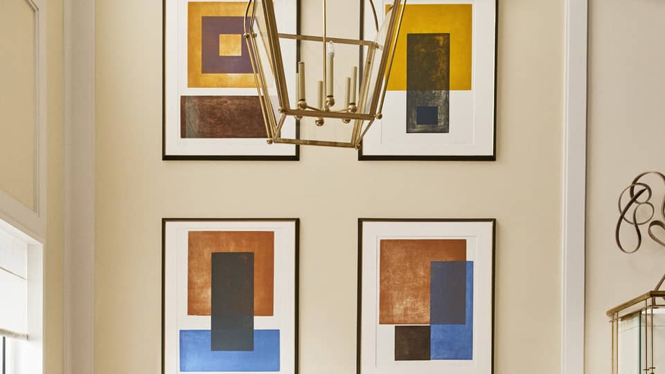 Luxury hotel seating area with a white round table and tan upholstered chairs beneath a chandelier, featuring abstract framed artwork on the wall