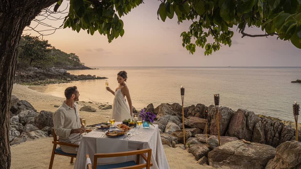 A beach dinner date at dusk, with a couple enjoying a serene seaside view.