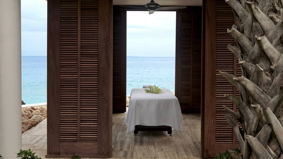 Massage table with white sheet under outdoor pavilion with wood shutters