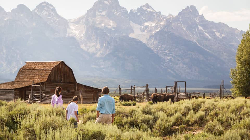 Family standing in a field with a cabin and mountains in the background.