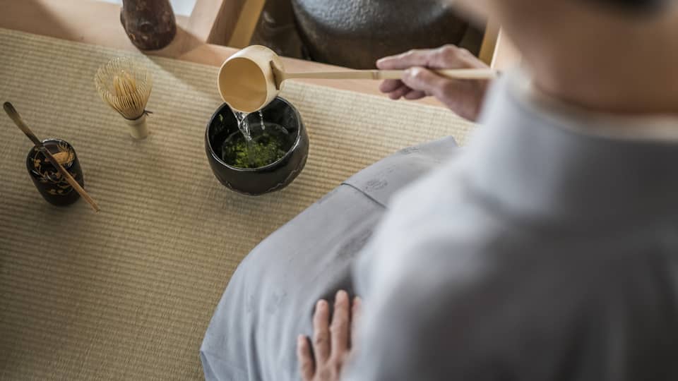 Woman kneels and pours tea from ladle during Tea Ceremony