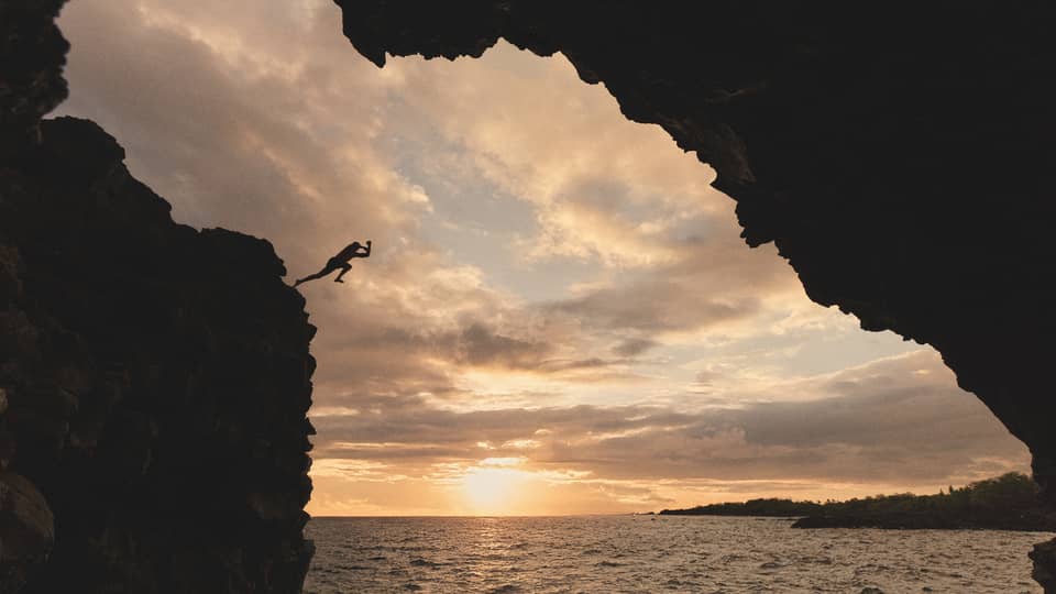 Person jumps off cliff into ocean at sunset in tropical destination