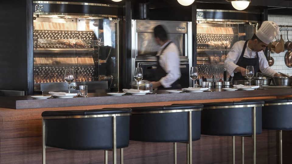 Chefs working behind a counter with black-and-gold stools in the foreground