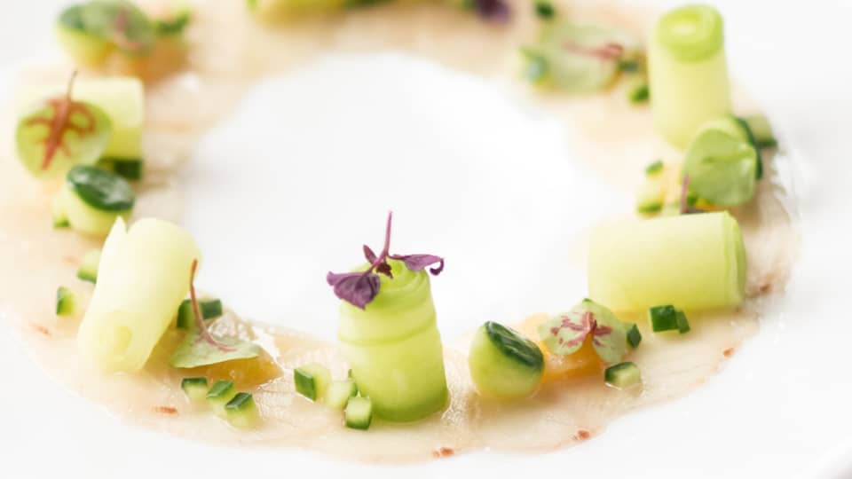 Round white dish topped with green vegetables and a light pink sauce