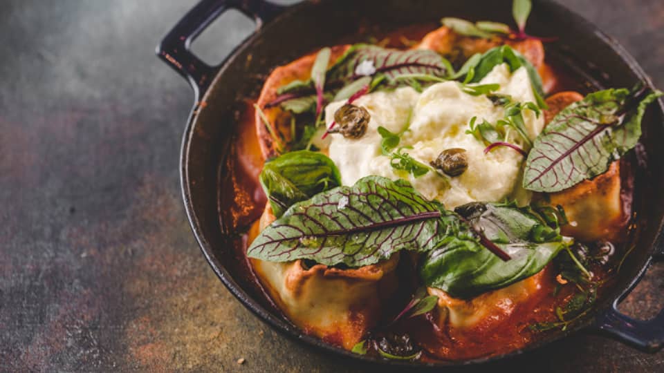 A pasta dish with a tomato sauce, and green leaves on top.
