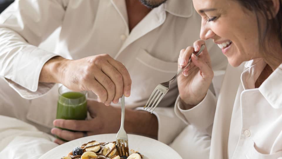 Two guests wearing pajamas and eating breakfast in bed